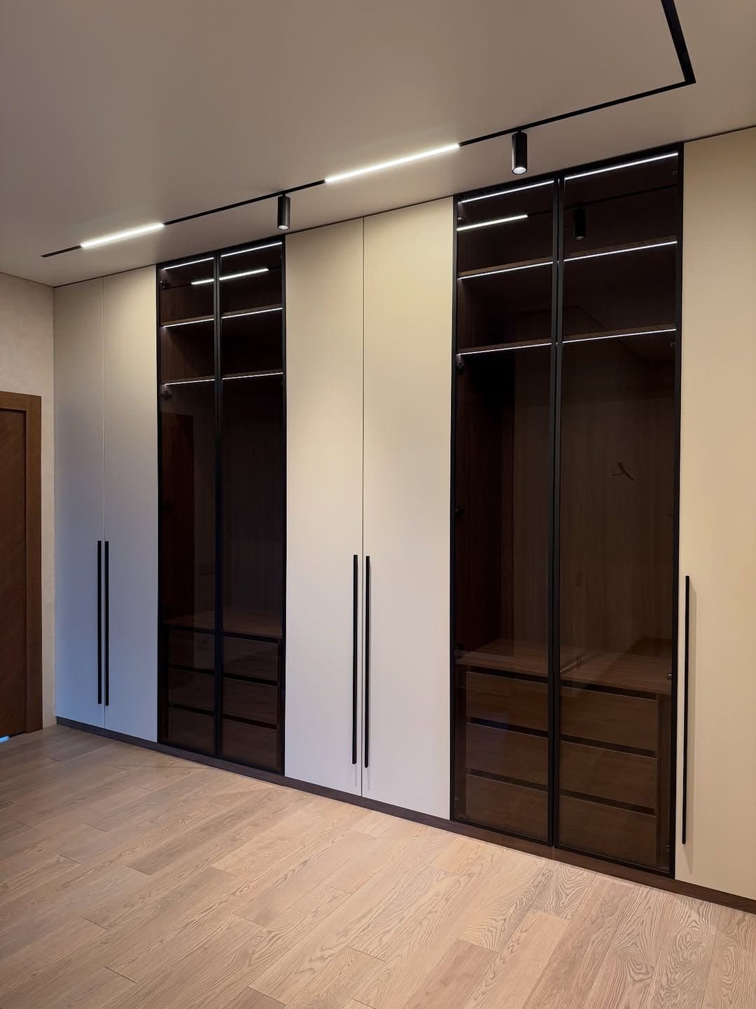 Cream wardrobe wall with bronze-tinted glass doors and brass-edged frames - bespoke joinery by Royalwoods Interiors, Nairobi