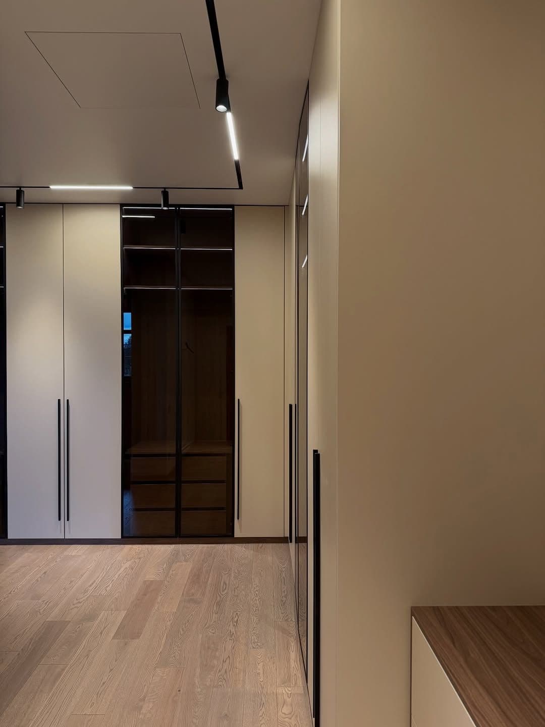 Handle-less cream wardrobe bank with smoked-glass display column, set against engineered oak flooring - bespoke joinery by Royalwoods Interiors, Nairobi