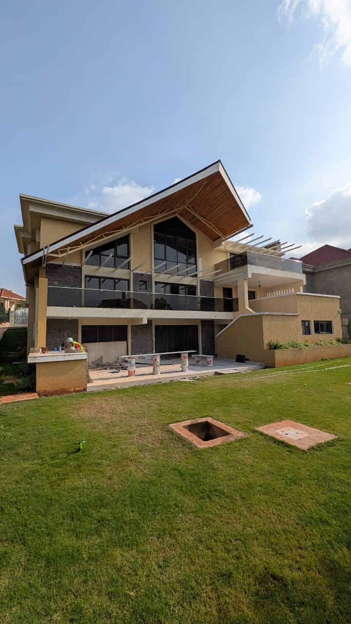 Rear elevation of a modern villa with mono-pitch timber-soffit roof, glass balustrades and fresh lawn - built by Royalwoods Interiors, Nairobi