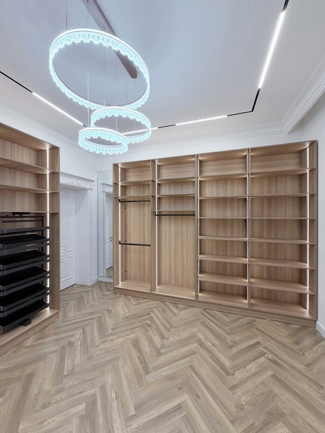 Light-oak walk-in closet under a crystal ring chandelier, laid on herringbone flooring - bespoke joinery by Royalwoods Interiors, Nairobi