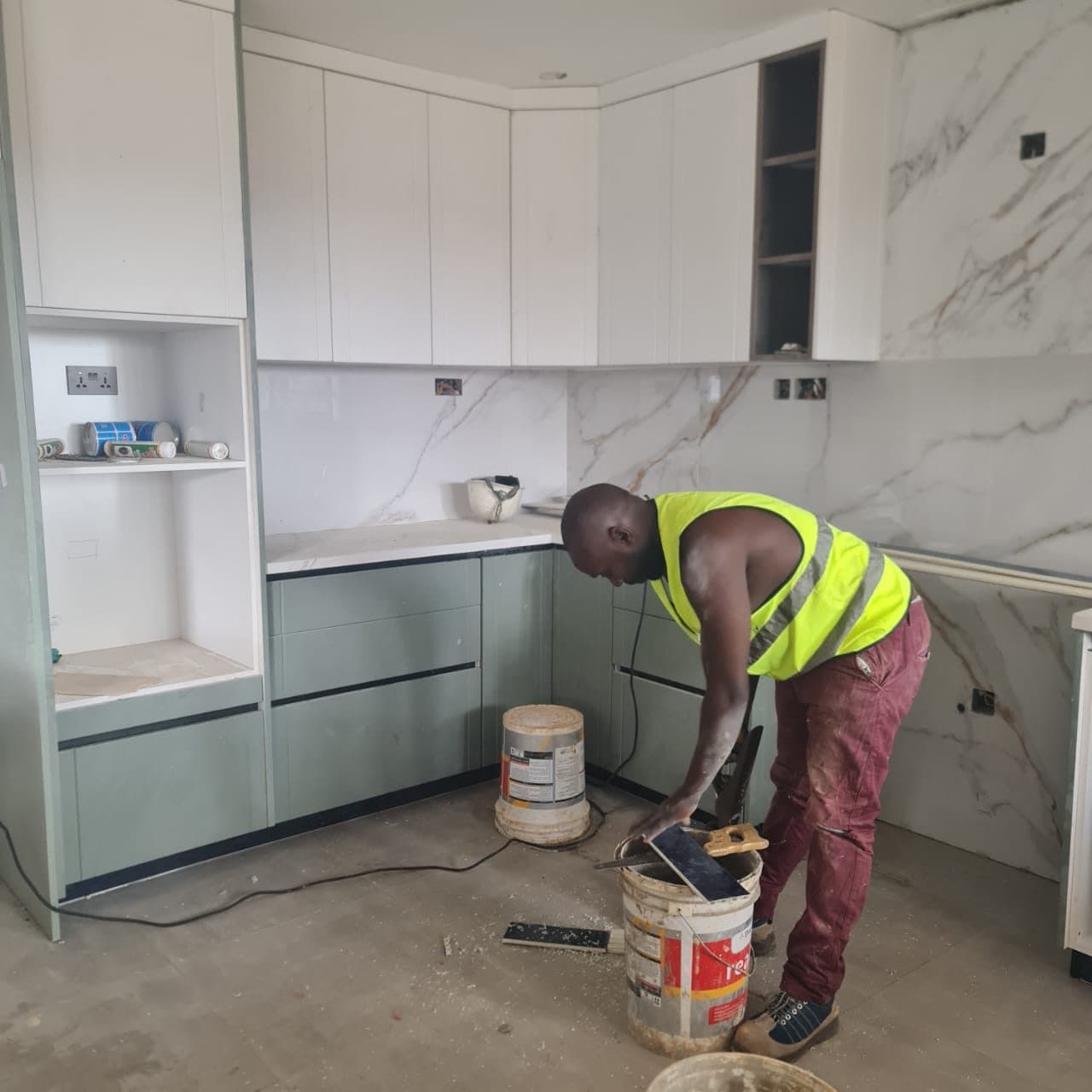 Sage-green kitchen being installed against a book-matched marble splashback at Tatu City