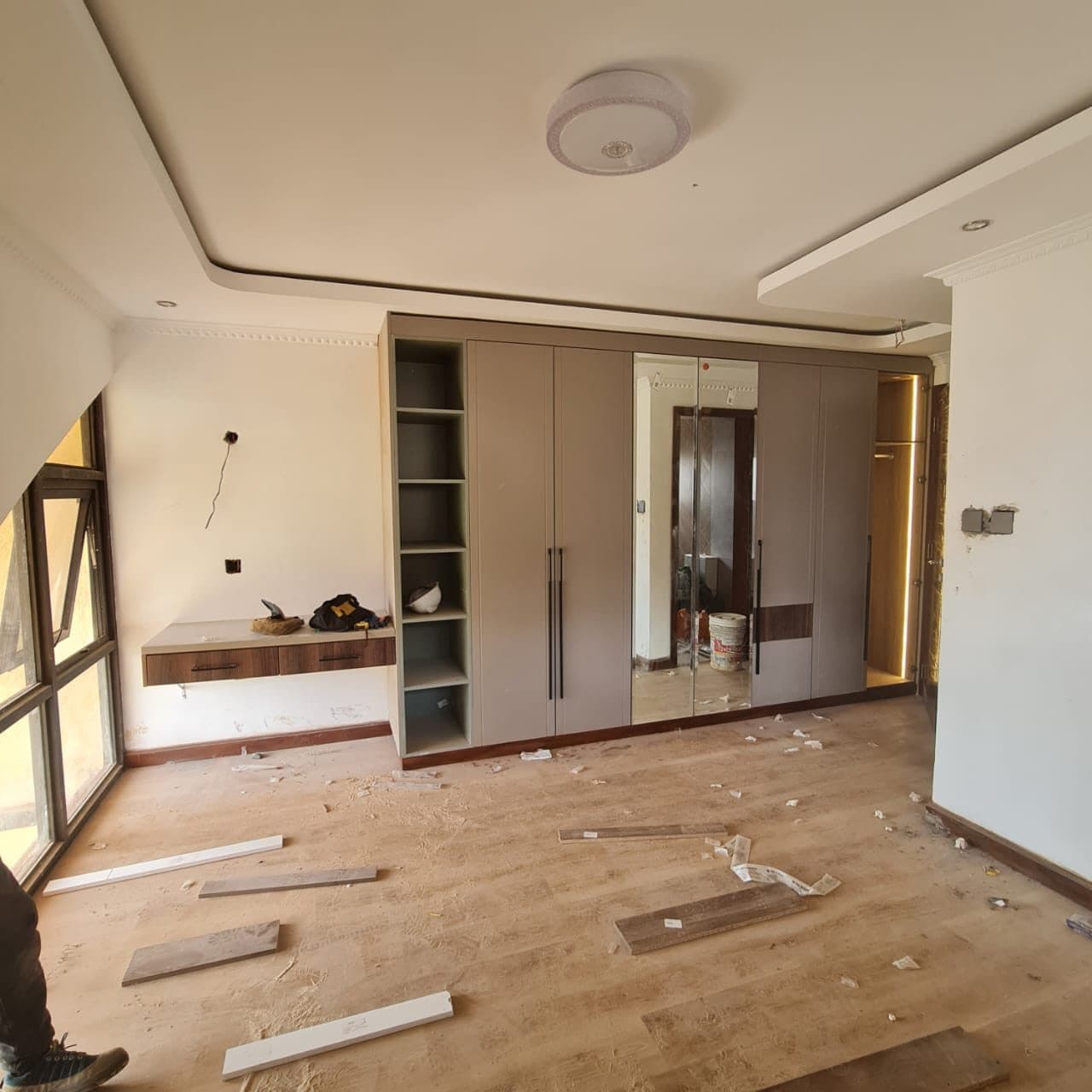 Taupe wardrobe bank with mirror panel nearing completion, protective debris still on floor - bespoke joinery by Royalwoods Interiors, Nairobi