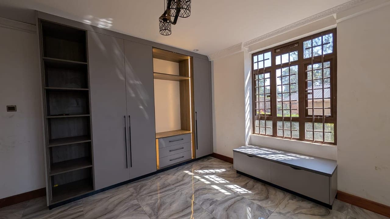 A bedroom wardrobe wall in warm grey, open shelving meeting a window bench - bespoke joinery by Royalwoods Interiors, Nairobi