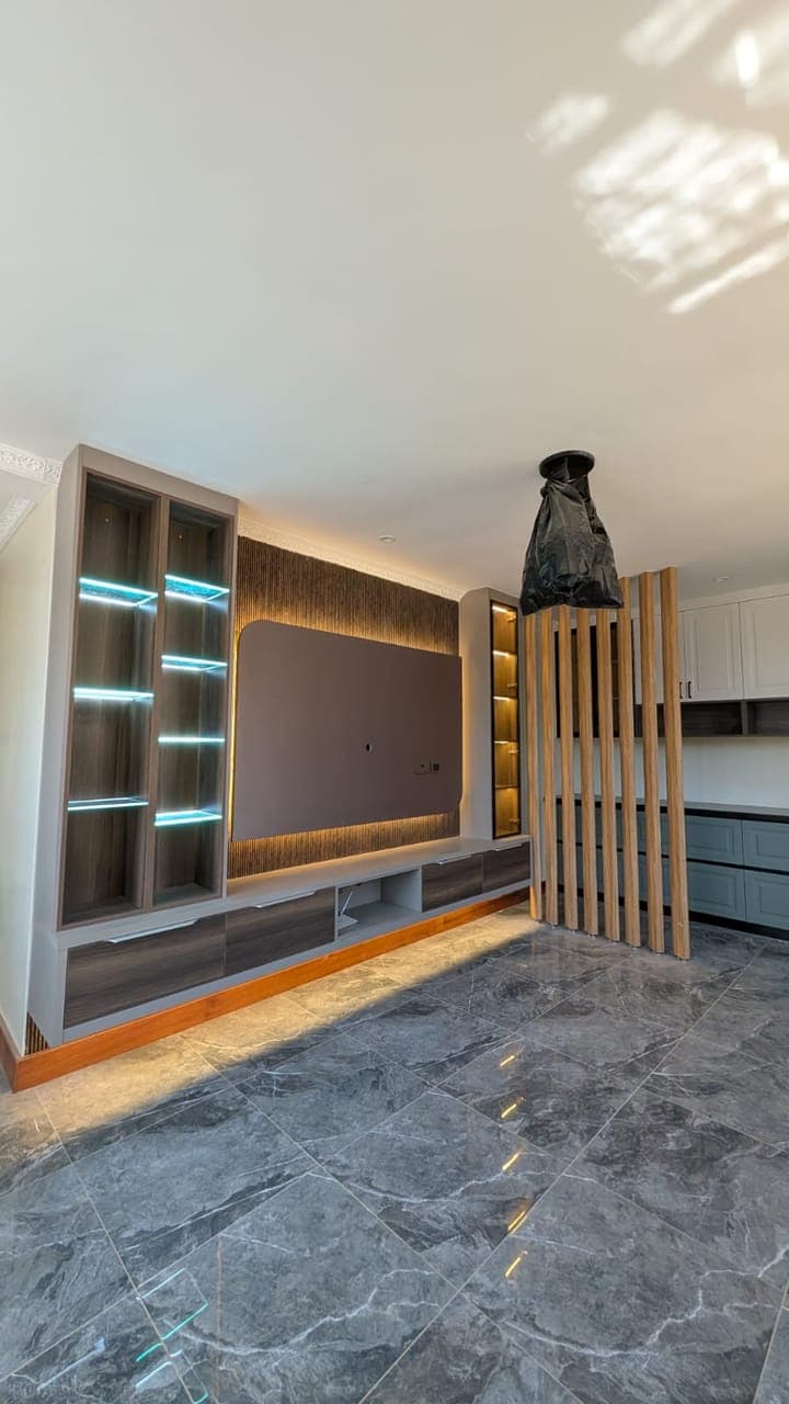 Media wall with blue-lit glass display cabinets and a fluted timber screen - bespoke joinery by Royalwoods Interiors, Nairobi
