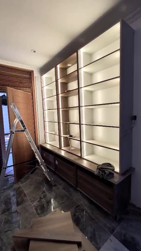 A full-height display wall with an LED channel in every shelf, set against dark timber and marble. — Royalwoods Interiors, Nairobi